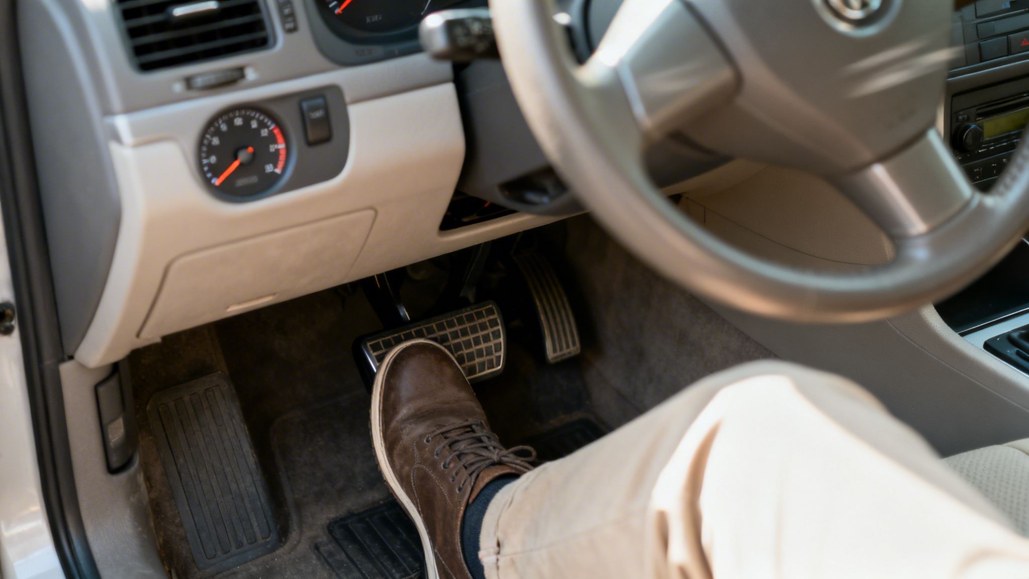 A person's foot in a brown shoe presses the car accelerator pedal inside a vehicle.