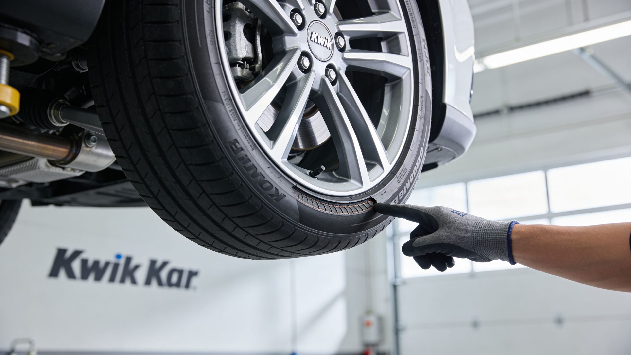 A mechanic wearing a glove points to a section of damaged tread on a vehicle's tire