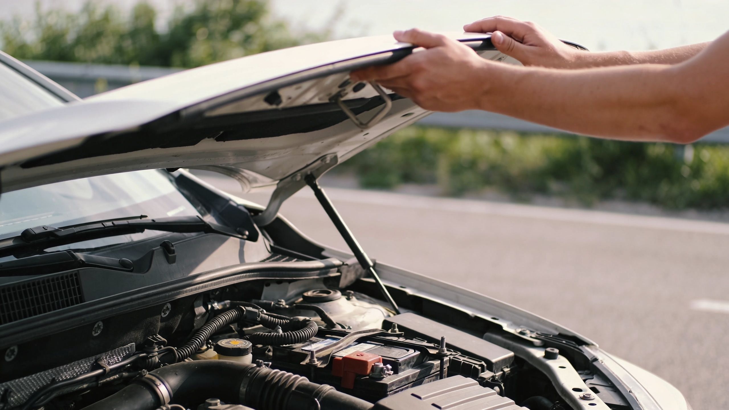 A person opening the hood of a car on the side of the road to check the engine.