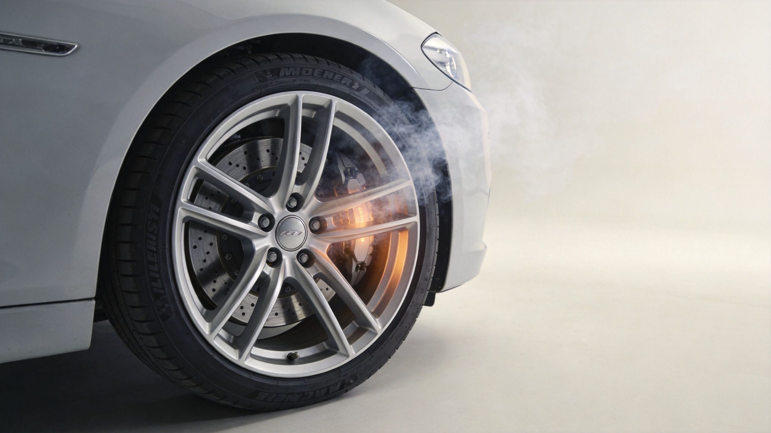 A close up view of a car wheel with a smoking hot brake caliper and rotor.