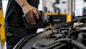 Hand pouring oil into car engine with dipstick nearby