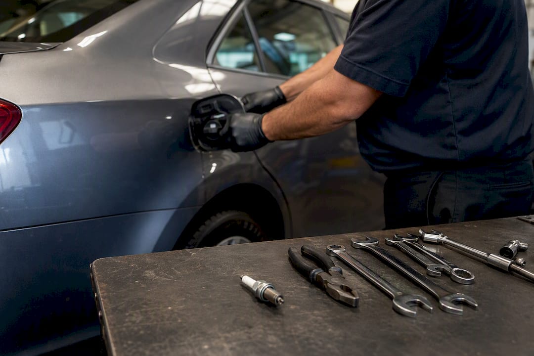 Hands tightening gas cap with spark plug and exhaust pipe nearby
